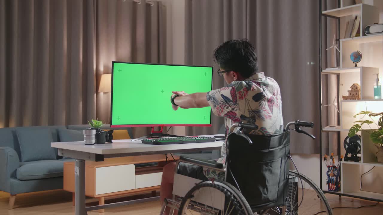 Back View Of Asian Man In Wheelchair Stretching While Using Mock Up Green Screen Desktop Next To The Camera At Home
