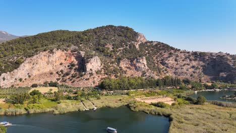 Drohnenaufnahmen-Eines-Bergtempels-Und-Der-Umgebung-Der-Stadt-Dalyan,-Die-über-Die-Felder-Und-Den-Bergfluss-Fliegen