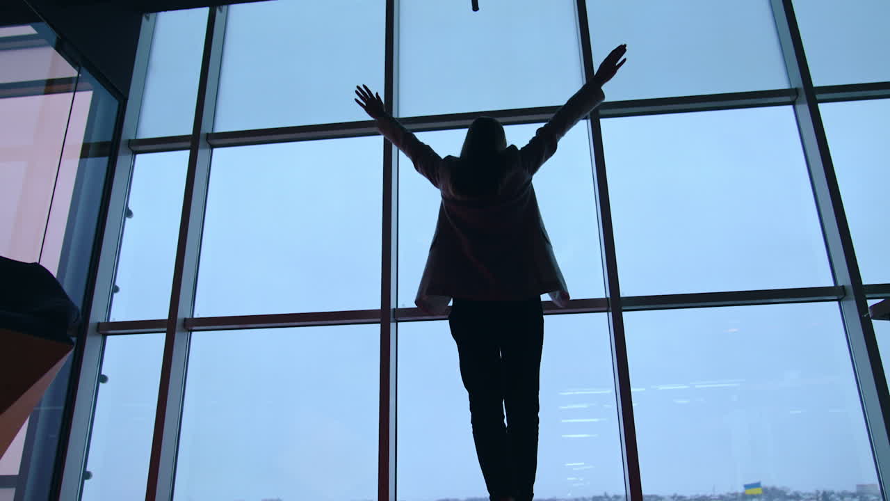 Lady in jacket and trousers comes up to the panoramic window. Dark female silhouette rises hands happily at the window.