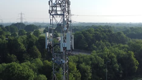 5G-broadcasting-tower-antenna-in-British-countryside-with-vehicles-travelling-on-highway-background-aerial-close-up-view