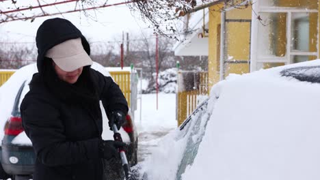 woman cleaning snow from car with brush - close up