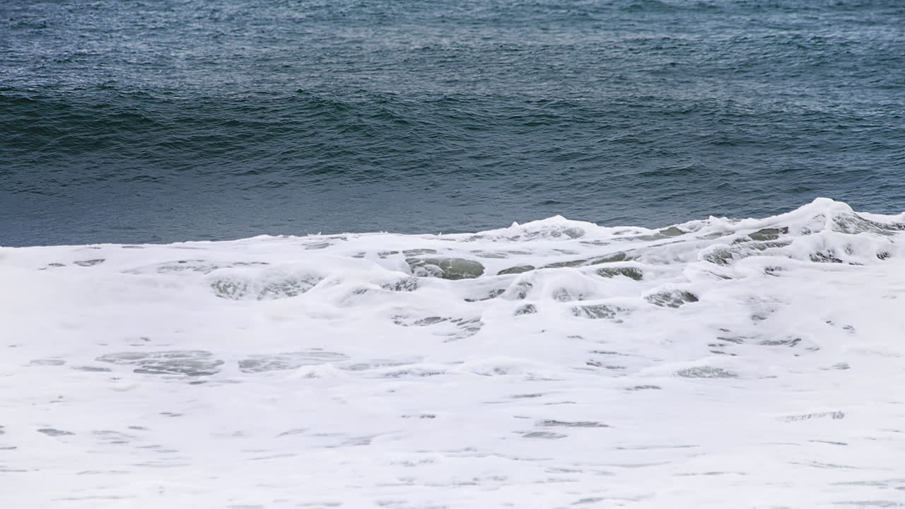 120fps 4k 푸티지에서 고속 카메라 120fps 4k 푸티지 뒤에 깊은 짙은 푸른 바다가 있고 하얀 물이 쏟아지는 해안에서 느린 동작으로 작은 파도가 형성되고 충돌합니다.