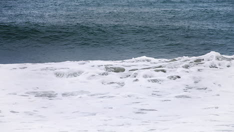 Small-wave-forming-and-crashing-in-slow-motion-in-the-shore-with-a-deep-dark-blue-ocean-behind-it-and-white-water-spilling-in-high-speed-camera-120fps-4K-footage