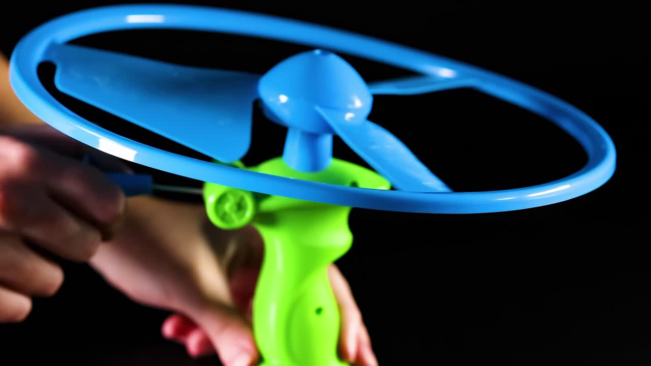 A detailed view of a hand launching a blue and green pull string toy against a black background.