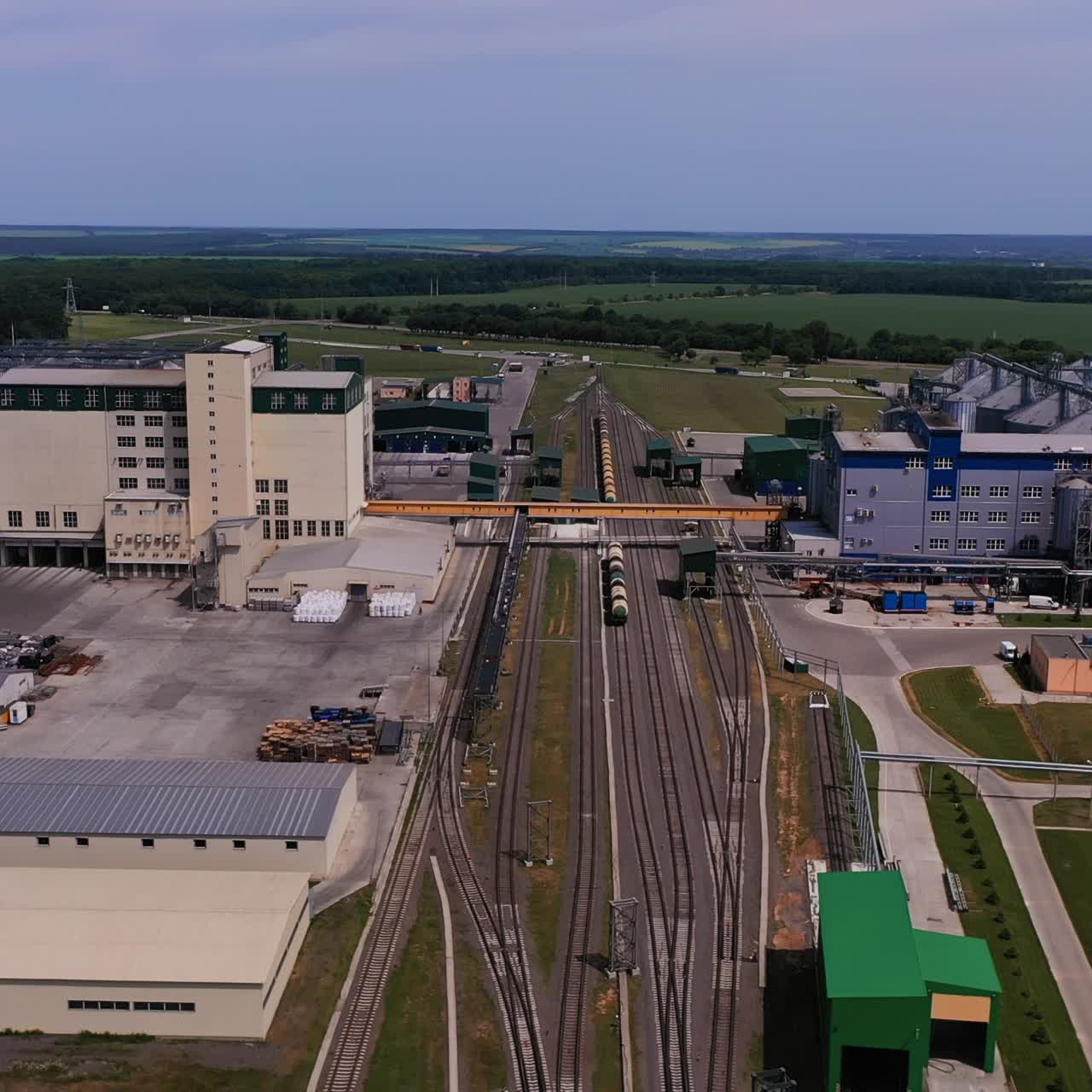 Railways with cargo trains crossing the industrial plant area. Elevator plant premises and silo containers on both sides of railways. Aerial view