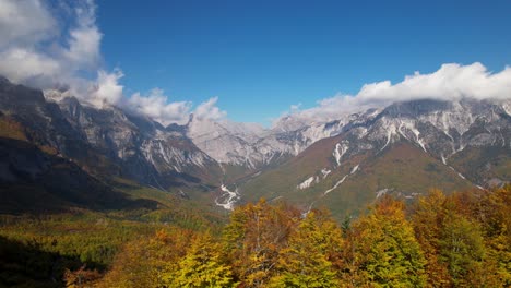 autumn landscape with golden leaves of trees and alpine mountain background, clouds and blue sky