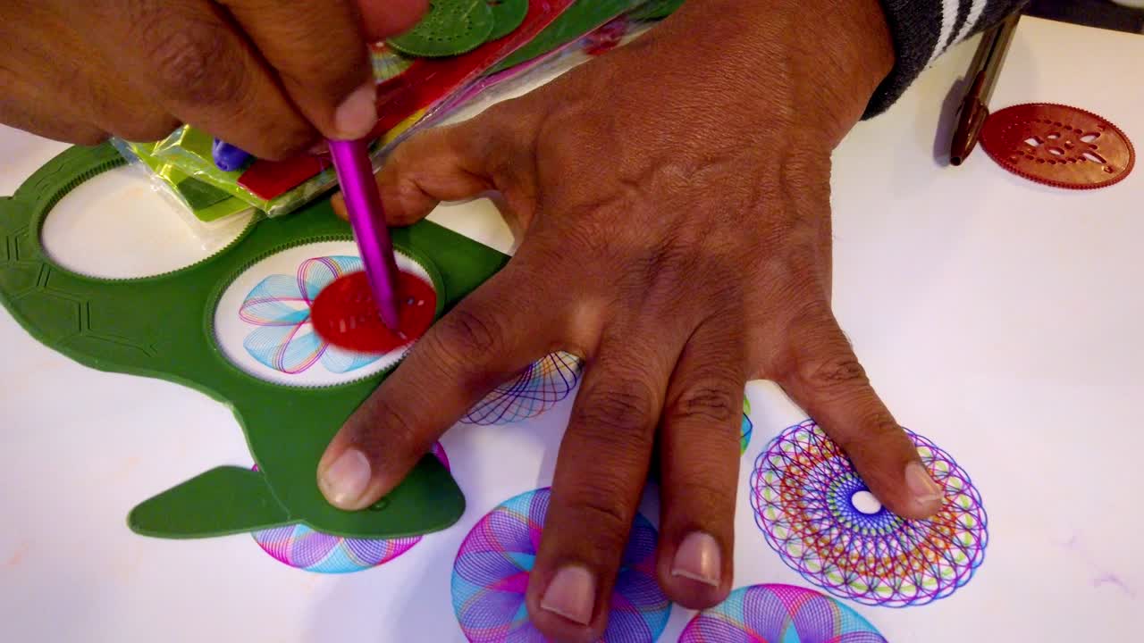 Vista dettagliata di una mano che crea complessi design geometrici con strumenti colorati su carta. Il primo piano cattura colori e texture vivaci, mettendo in mostra la precisione artistica