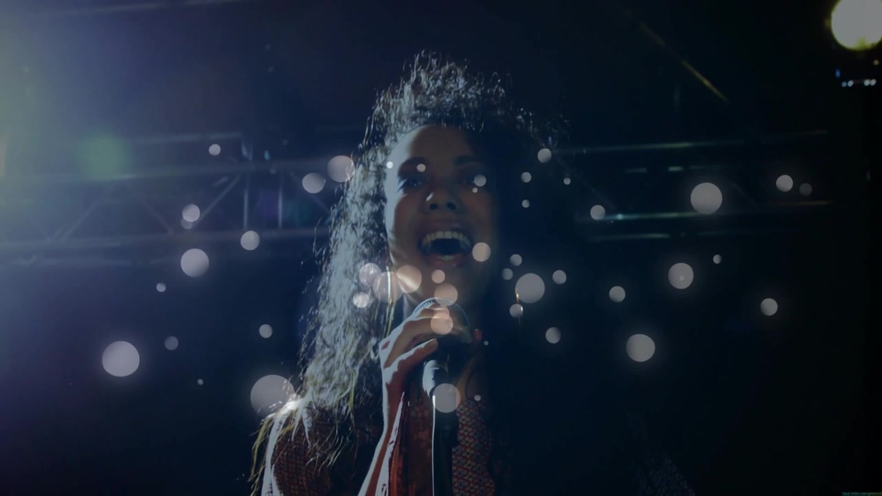 Female singer performing on dark music stage, singing into mic and causing layered bokeh building