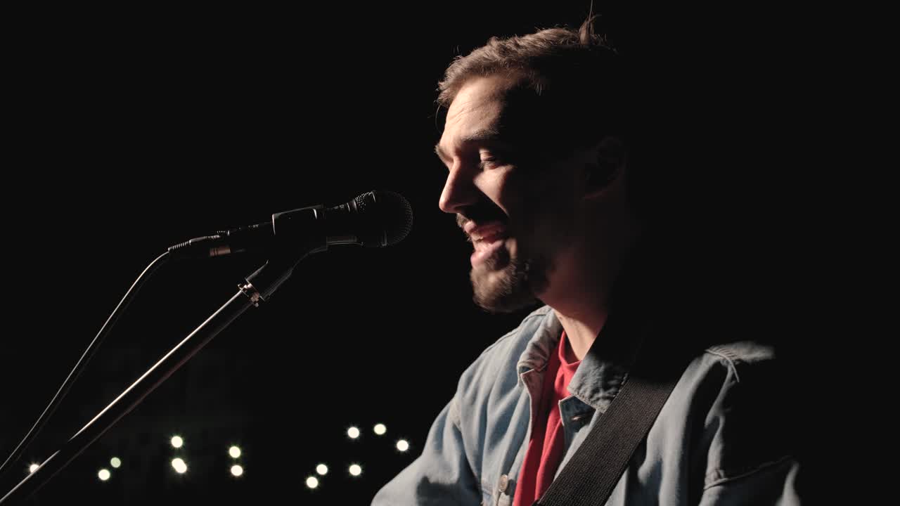 un músico está tocando la guitarra en un gran escenario con miembros de la audiencia sosteniendo linternas en el fondo. el auditorio está lleno de hermosas luces parpadeantes.