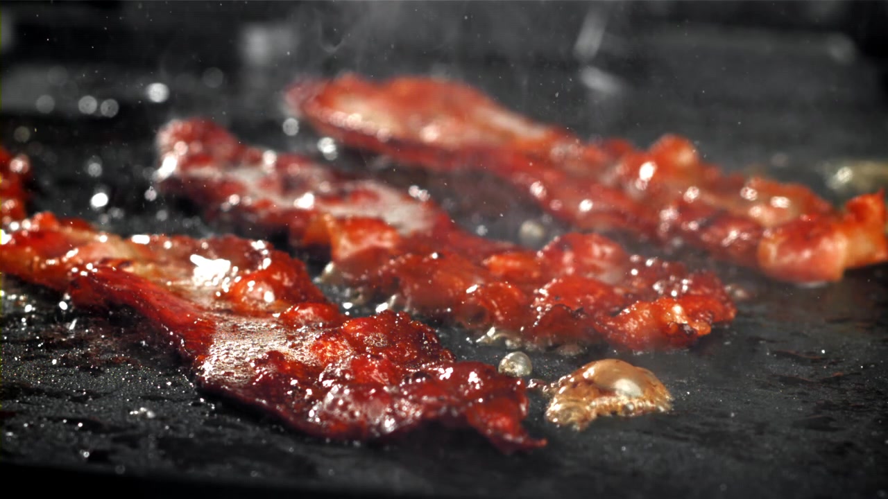 Strisce di pancetta deliziose che friggono su una piastra calda