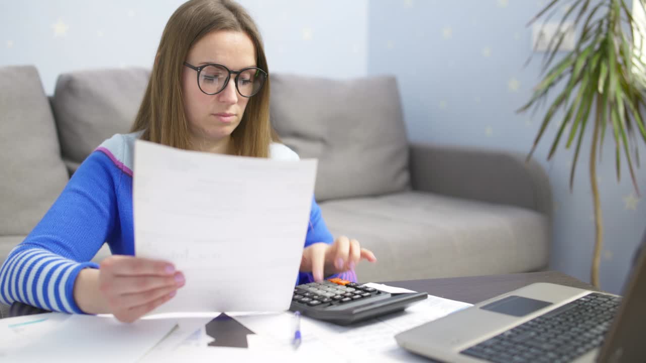 mujer usando calculadora para calcular facturas domésticas en el hogar, haciendo papeleo para pagar impuestos