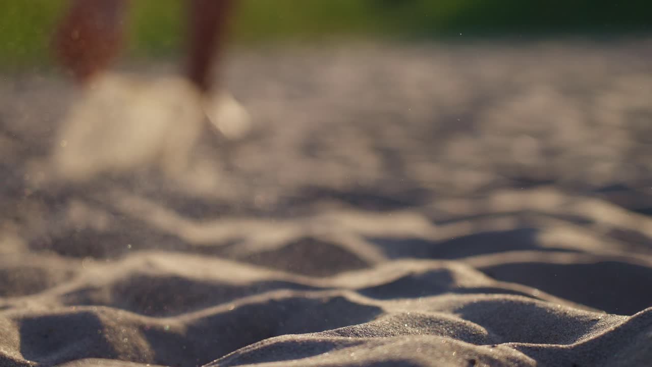 Bare feet running through soft sand, close-up shot with sand grains flying.