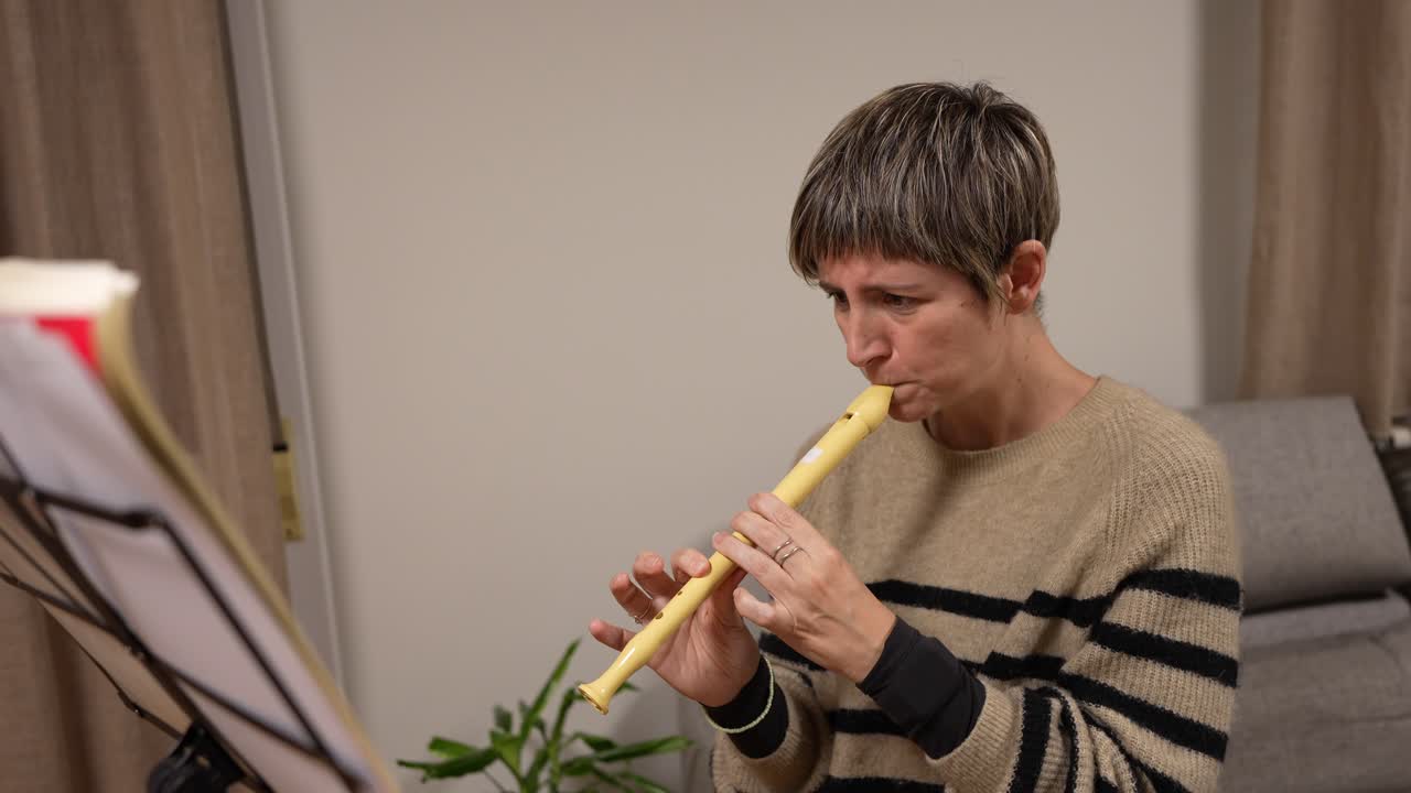 Mujer concentrada tocando un instrumento musical, la flauta dulce, en casa