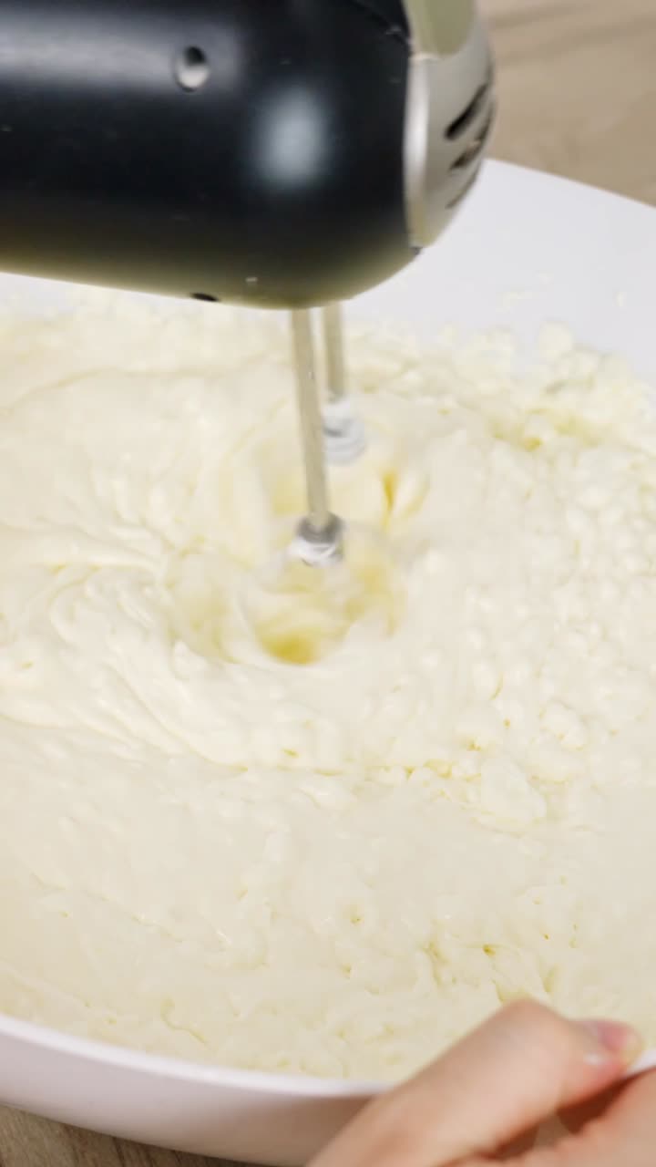 Electric hand mixer spread back and forth across white bowl to create stiff peaks, vertical