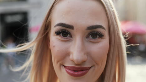 Close-Up-Of-The-Smiling-Blonde-Happy-Young-Woman-Laughing-Cheerfully-While-Looking-At-The-Camera-And-Her-Hair-Waving-On-The-Wind