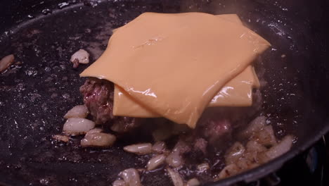 Rebanadas-De-Queso-Añadidas-A-La-Hamburguesa-En-Una-Sartén,-Cocidas-Con-Cebolla,-Primer-Plano.