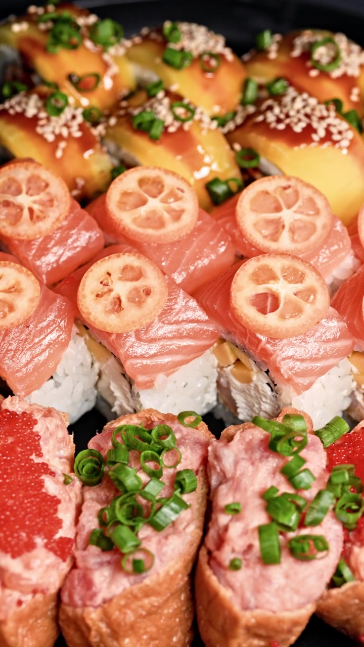 新鮮な魚と彩り豊かなトッピングが施され、レモンのスライスとゴマが見える巻き寿司が黒い皿に盛り付けられている。
