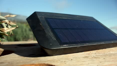 Pan-shot-of-a-small-solar-panel-placed-on-a-wooden-surface-out-in-the-sun