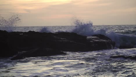 rough sea with waves breaking against rocks in the sea, in a sunset