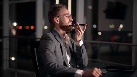 Happy-young-man-in-business-suit-talking-on-the-phone-sitting-at-the-table