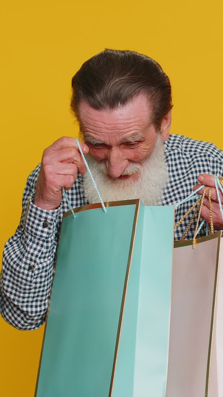 Happy senior old man shows shopping bags advertising discounts amazed with low prices holidays sale