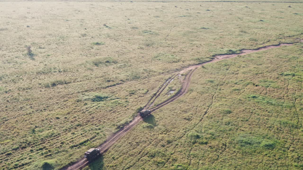 Aerial view of two safari vehicles driving along a trail in the Serengeti