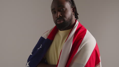 studio portrait shot of man wrapped in american flag celebrating 4th july independence day 2