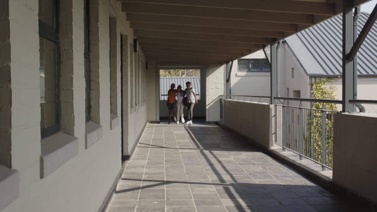 Multiracial students walking together in school hallway, enjoying conversation, copy space