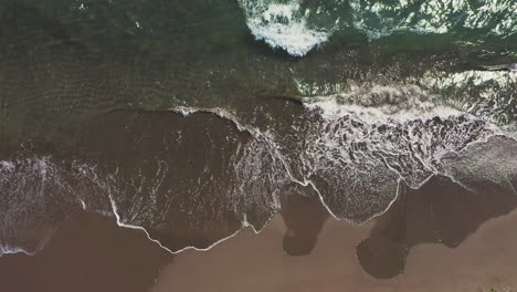 aerial view of waves crashing on a dark sand beach