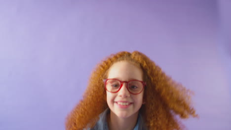 studio shot of young girl with red hair and glasses jumping against purple background