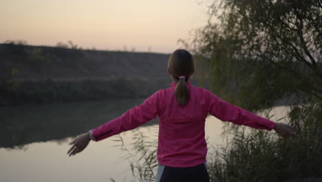 woman stretching and practicing yoga by a river at dusk