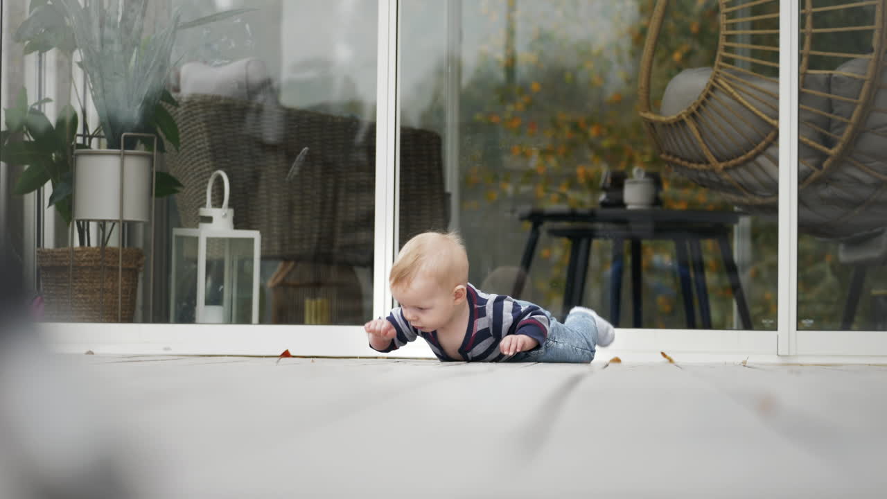A blonde baby boy struggles to crawl on a porch, falling gently while exploring the outdoors