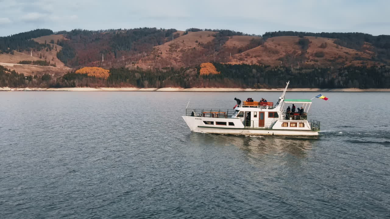 Aerial drone view of a boat with people floating on the Bicaz lake in Romania. Hills covered with lush forest