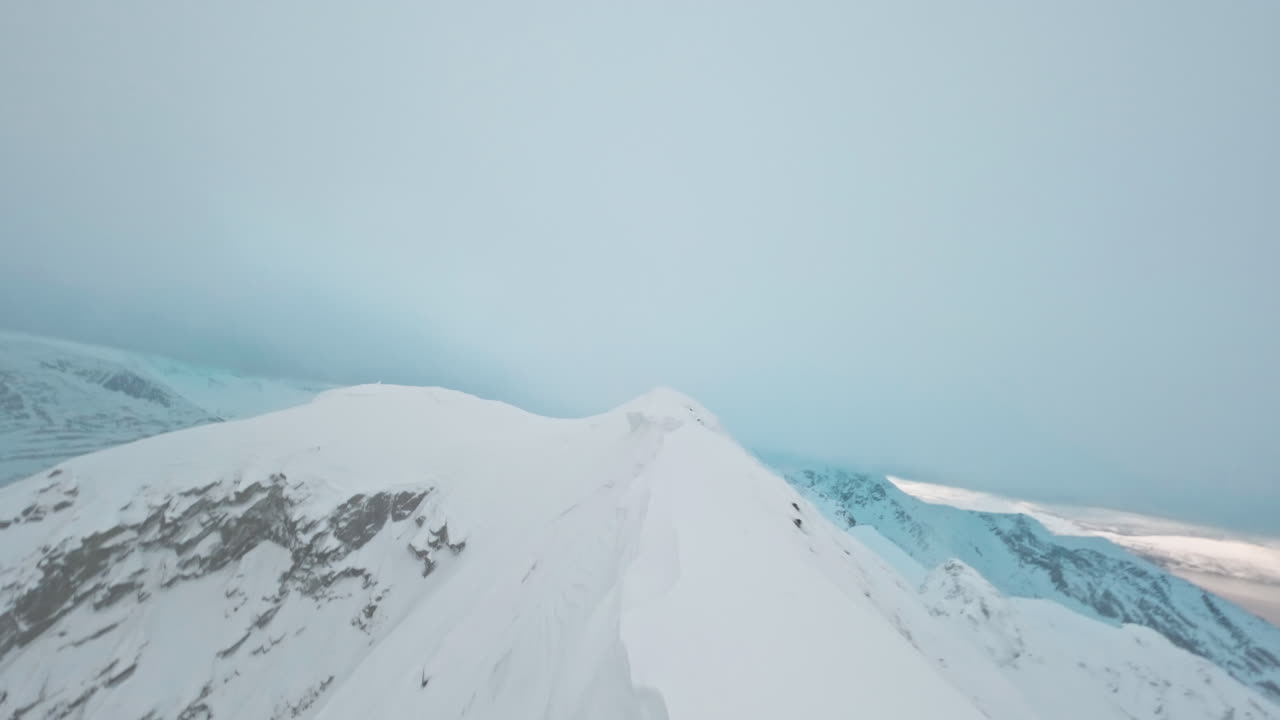 Snow-covered mountain ridge with fjord view under misty sky, Tromsø, Norway