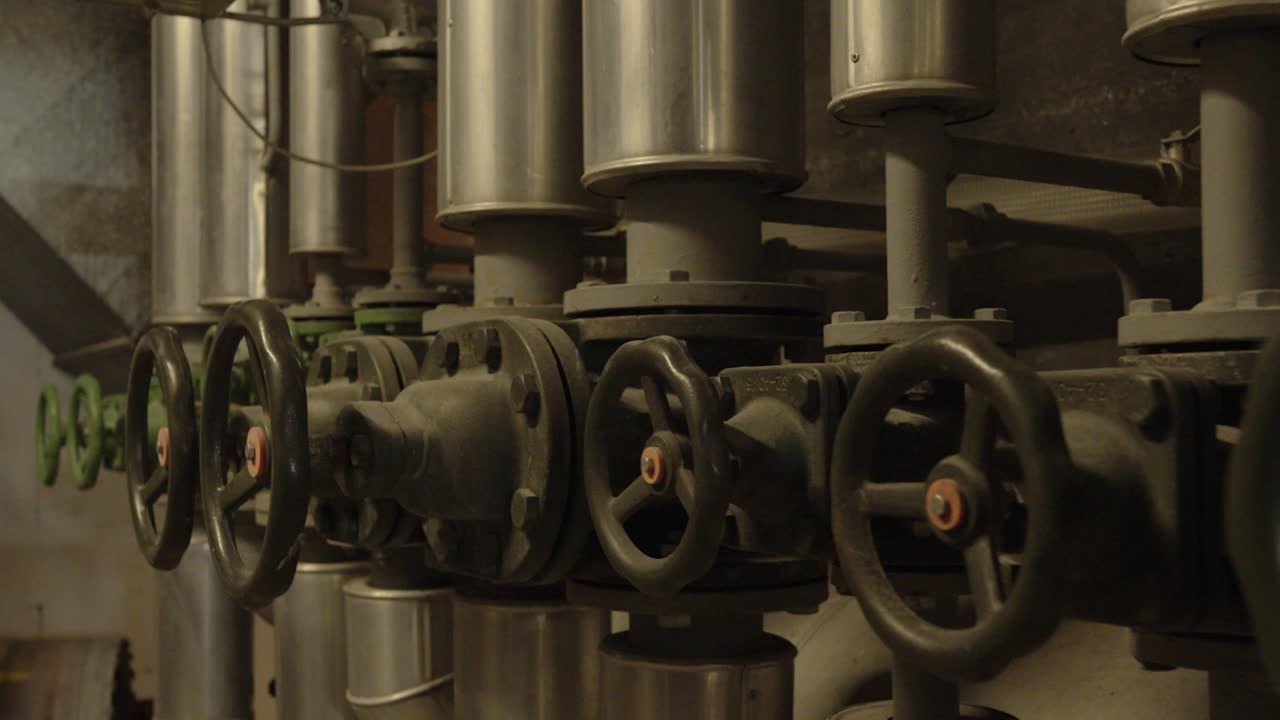 Close-up of multiple industrial valves connected to large metal pipes inside a technical facility. Concept for engineering, machinery, energy, and infrastructure