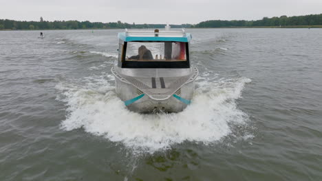 blond girl driving silver aluminum boat over river with trees on riverbank filmed with drone close up from front