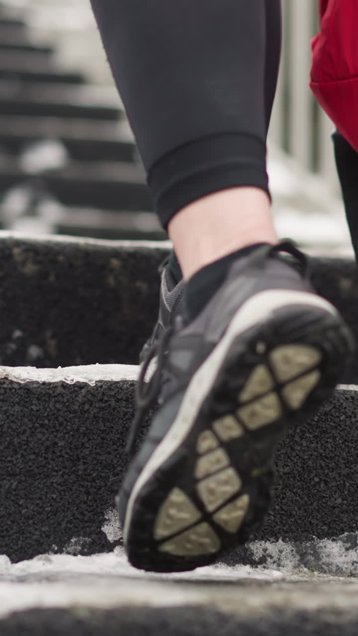 close-up of legs in sneakers walking up snowy staircase while carrying red backpack, snow-dusted stairs with iron railing by the side and athletic footwear, showing winter outdoor activity