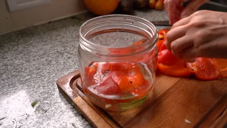 putting chopped red bell peppers into jar with oil and water. food preservation. close up