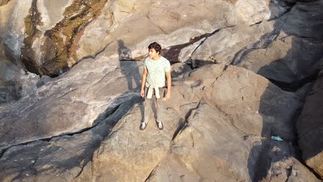 aerial view or drone shot of a young asian boy standing on a cliff of small mountain made with rocks in forest near a small waterfall video background