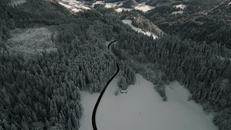 Cars-on-a-street-in-a-mountain-valley-in-idyllic-snowy-landscape-with-trees-and-snow