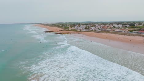 Aerial-pan-across-playa-el-palmar-surfers-in-beautiful-ocean-blue-water-at-sunset