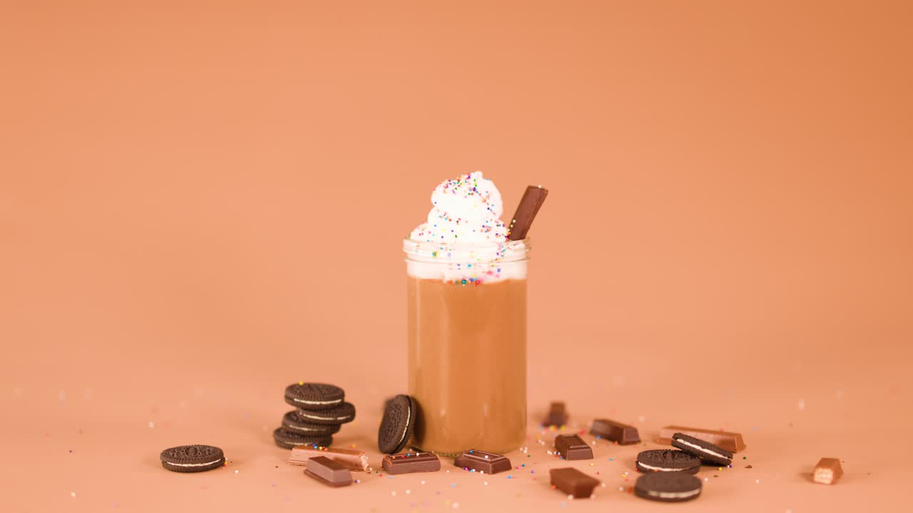 Chocolate syrup drizzled onto whipped cream-topped milkshake, surrounded by cookies and candy, studio lighting