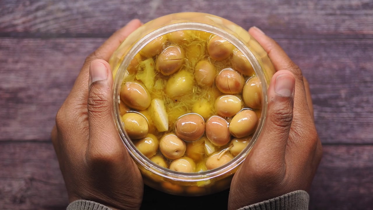 Hands Holding a Jar of Pickled Green Olives with Garlic and Ginger