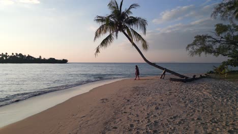 chica de yoga se pone de pie bajo las palmeras en la playa de ensueño