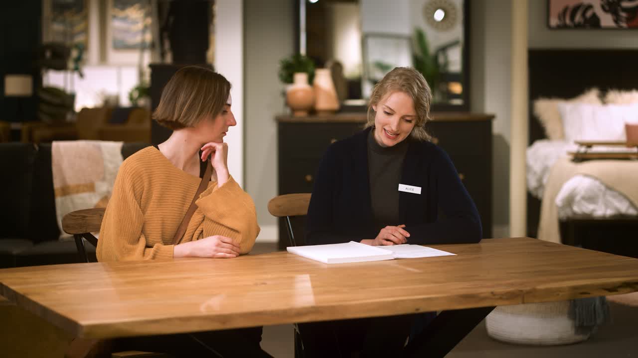 Due donne sedute confrontano offerte, commessa e cliente in negozio