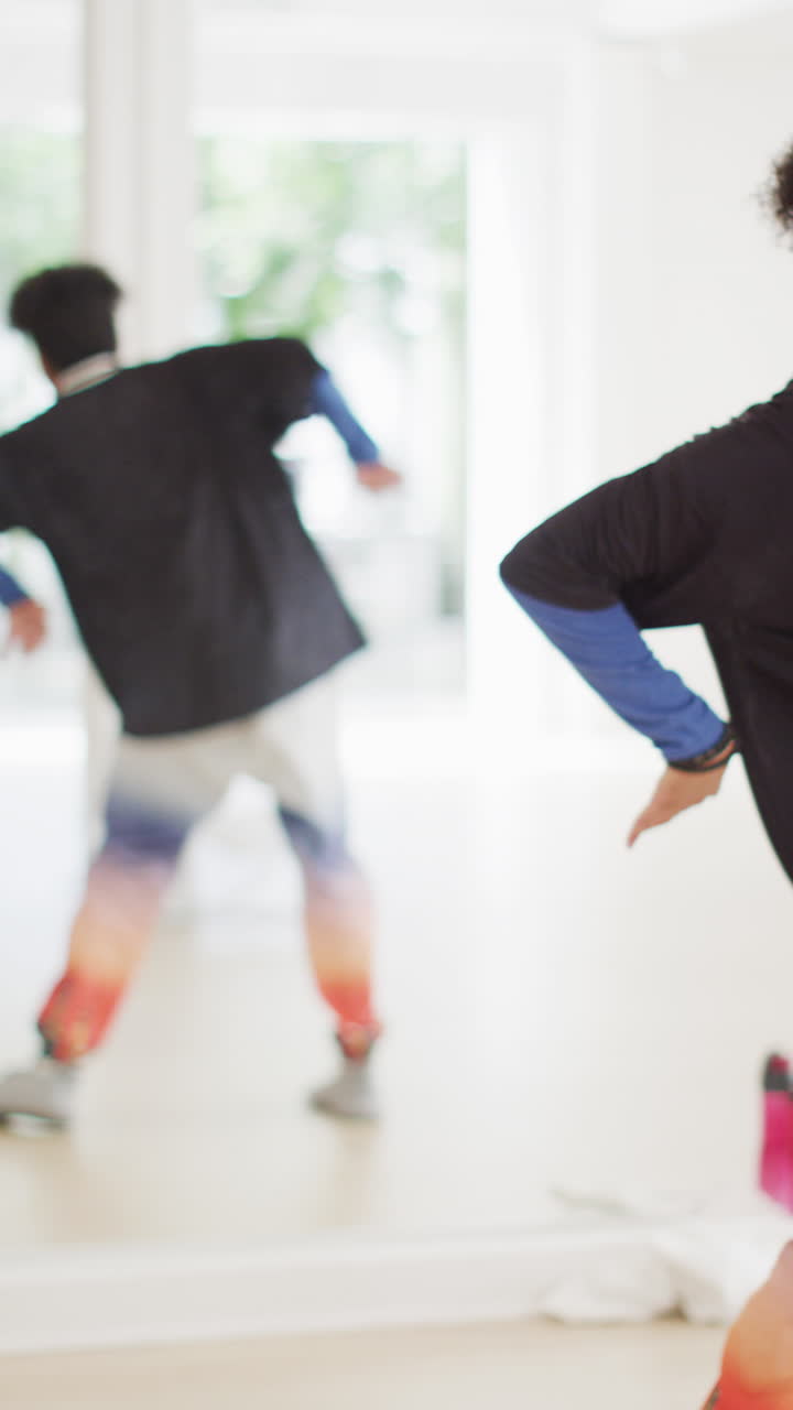Vertical video of happy biracial male dancer dancing in front of mirror in dance studio