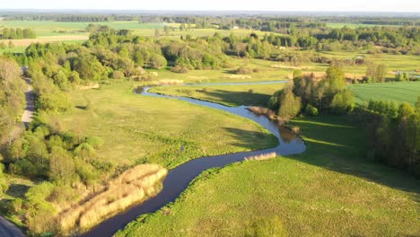 Slow-aerial-dolly-push-in-above-calm-river-meandering-bends-and-reeds-growing-along-edge