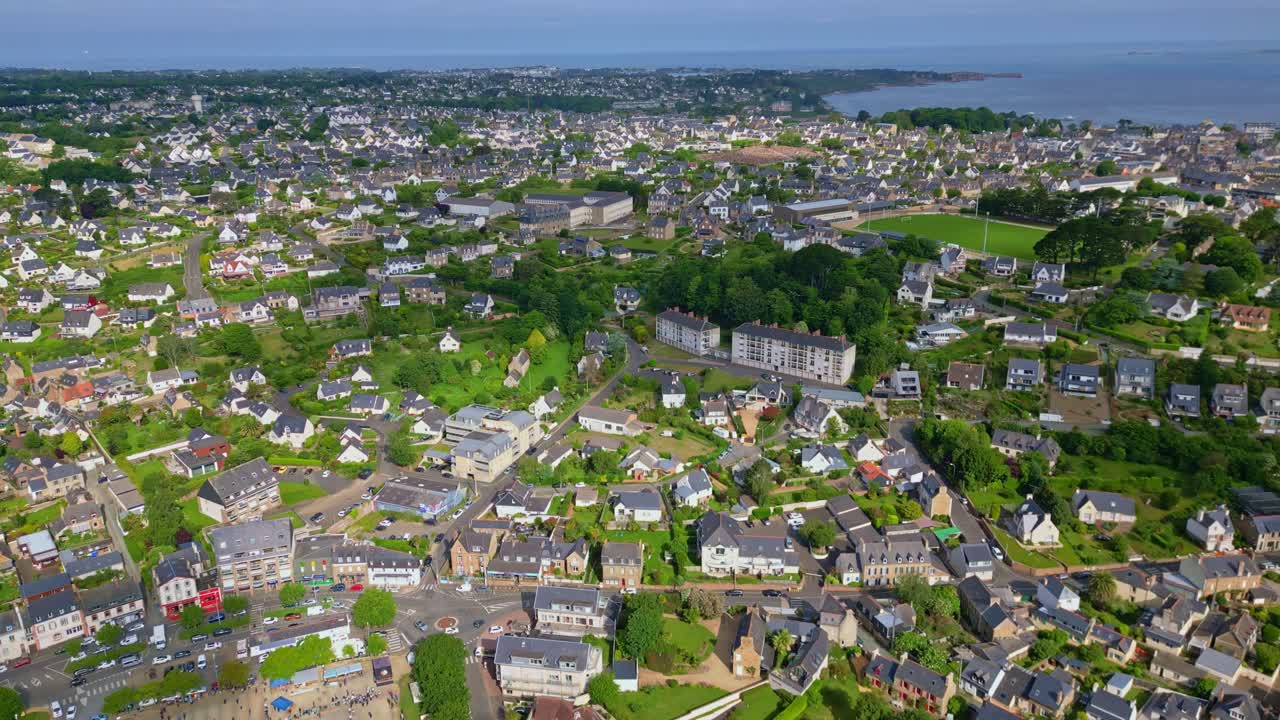 Perros-Guirec coastal town, houses, green spaces, and sea in background, Brittany, France. Aerial drone sideways