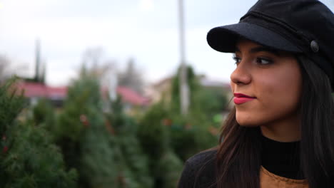 a hispanic woman shopping on a christmas tree lot with green fir conifers in a seasonal holiday nursery