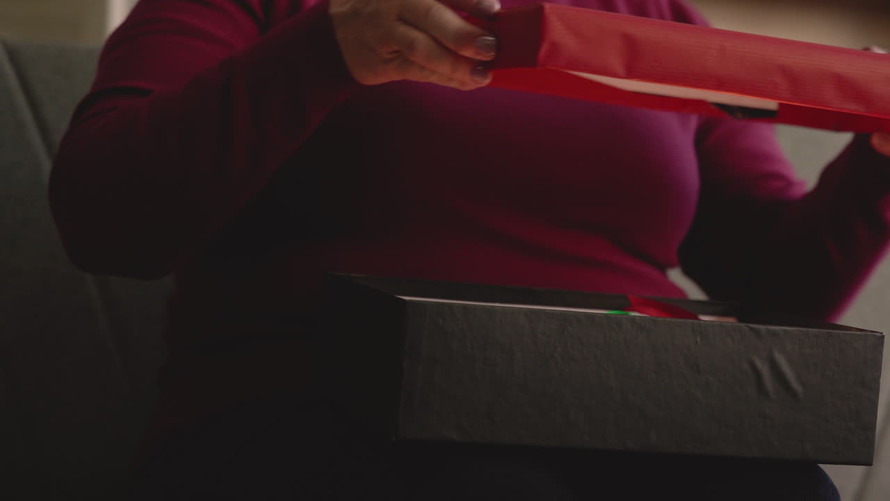 소파에 앉아 있는 상자에서 크리스마스 선물을 꺼내는 여성의 손을 가까이서 볼 수 있습니다.